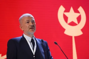 Андрій Мельниченко виступає на трибуні з мікрофонами на тлі червоного логотипу