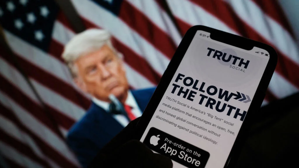 Смартфон з екраном Truth Social «FOLLOW THE TRUTH» на тлі Дональда Трампа та американського прапора, ілюстрація до планів Trump Media продавати доступ до постів за 100 тисяч доларів.